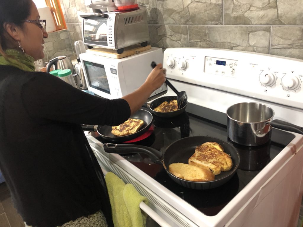 Malena making French toast for 4 people with gigantic French bread that barely fit in the pan. She improvised and cooked with three pans at once, and only burned a few spots.